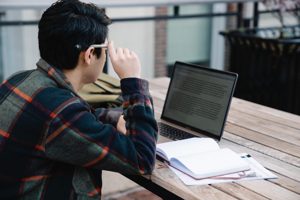 Man sitting at picnic table with a notebook and laptop computer